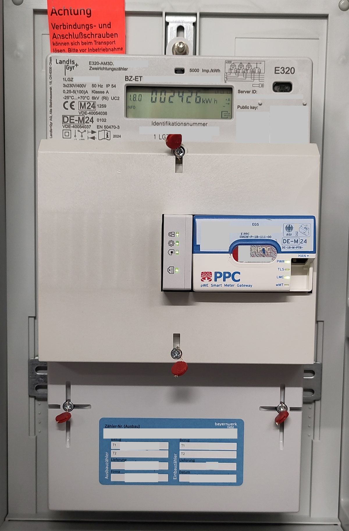 Zählerschrank mit Zweirichtungszähler, Smart-Meter-Gateway und einem blauen Aufkleber unten, der Felder für Ausbauzähler und Einbauzähler mit Bezug T1 und T2, Lieferung, Firma und Datum enthält